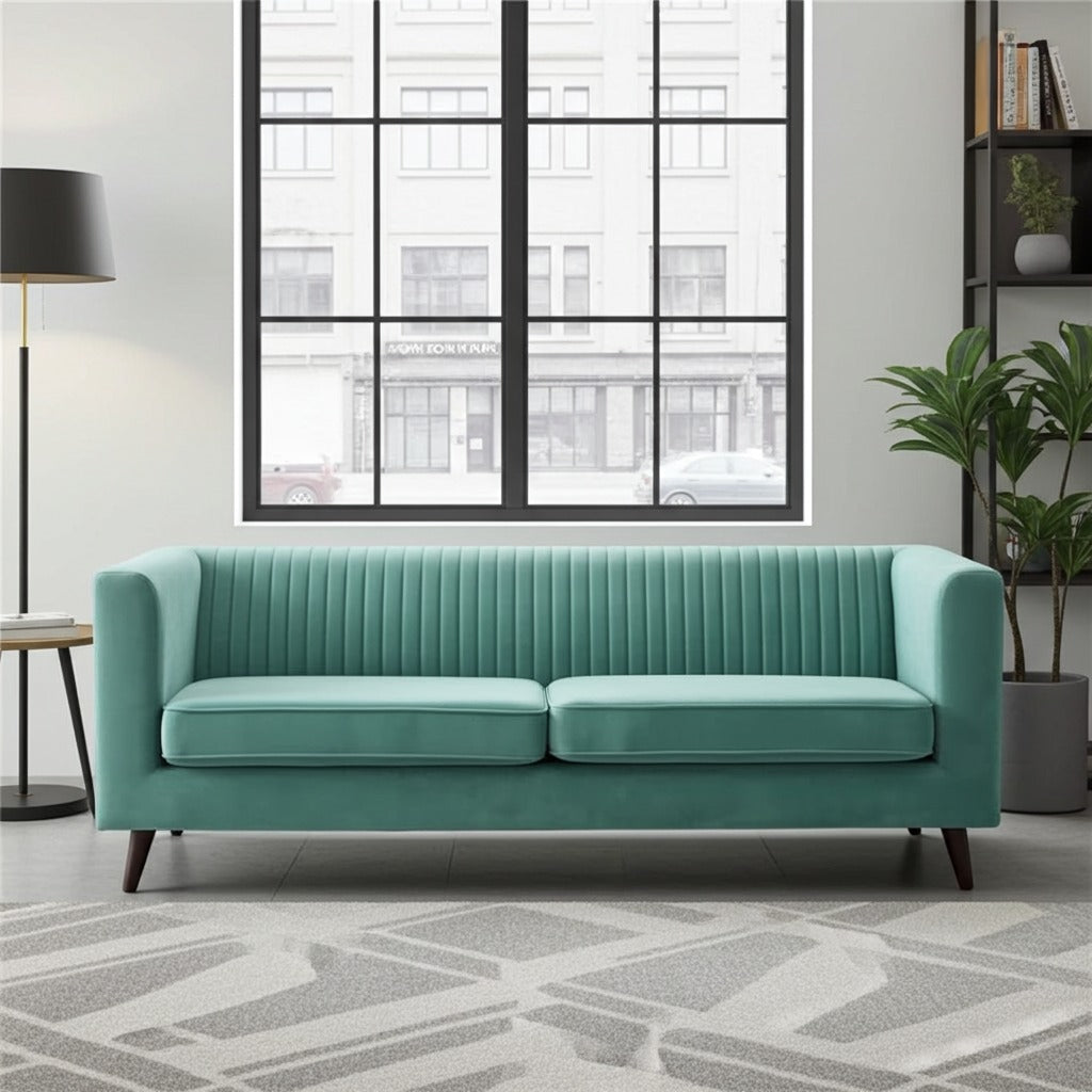 A mint green velvet loveseat sofa with vertical channel tufting on the backrest, shown in a modern living room setting with a gray patterned rug, a black floor lamp, and a window view.