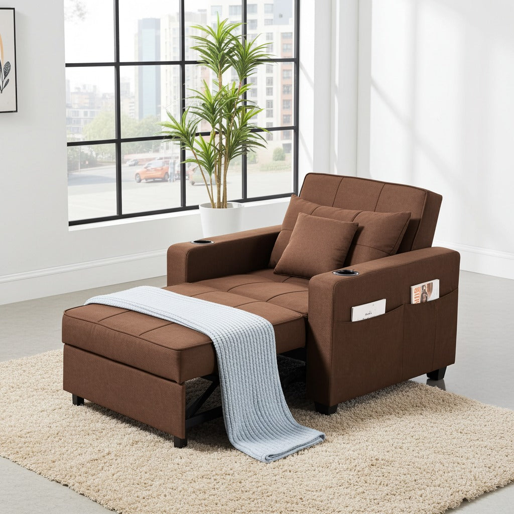 A brown fabric recliner sofa chair with an ottoman base, shown in a bright modern room with a large window, potted plant, and beige rug. The chair has two matching brown pillows, side cup holders, a side pocket holding a magazine, and a light blue knit throw blanket draped over the front.