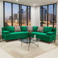 A bright green sectional sofa with four colorful patterned accent pillows, set in a modern living room with a glass-top coffee table, white rug, and large windows overlooking a city skyline at dusk.