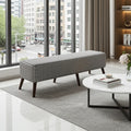 A rectangular upholstered bench with a black-and-white houndstooth pattern and dark tapered legs, placed in a bright modern living room beside a round white coffee table and large floor-to-ceiling windows.