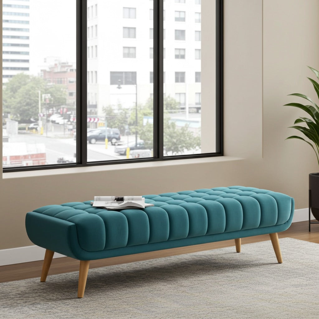 A teal tufted velvet bench with light wood legs, styled in a modern room with a large window showing an outdoor city view.