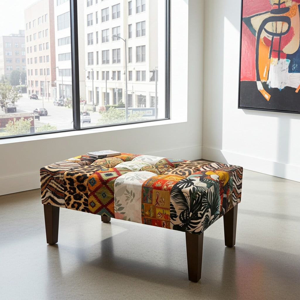 A rectangular upholstered ottoman bench with dark wooden legs, featuring a vibrant patchwork of animal and geometric prints, set in a modern room with a large window.