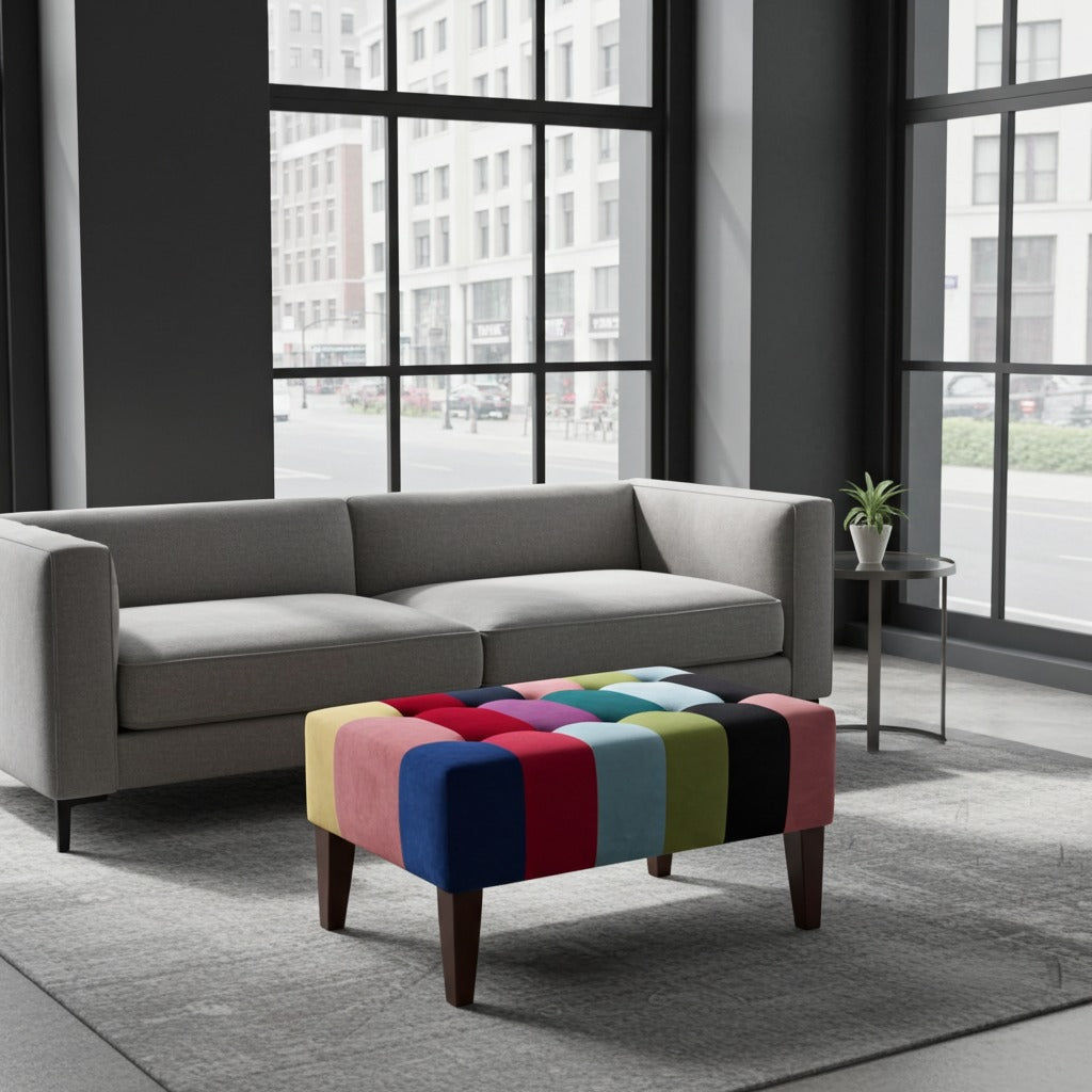 A modern gray fabric sofa in a bright, contemporary room with large windows, styled with a colorful tufted ottoman featuring a patchwork of red, blue, yellow, green, pink, and black cushions.