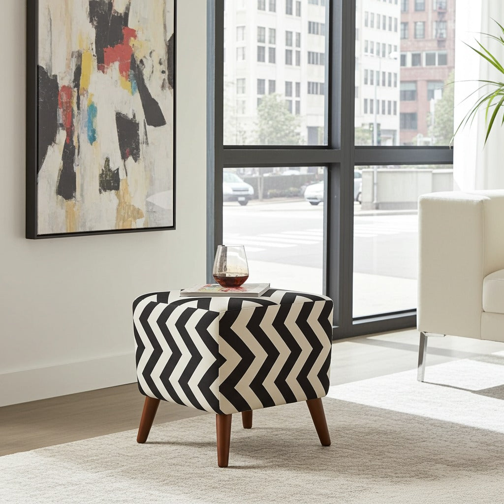 A round upholstered ottoman with a bold black and off-white chevron pattern and four wooden legs, styled in a modern living room setting next to a window.