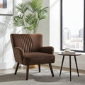 A brown upholstered accent chair with vertical channel tufting on the backrest, shown in a modern living room setting next to a small round side table and a potted palm plant.
