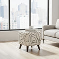 A square ottoman with dark legs and a cream upholstery covered in a black abstract line pattern, styled in a modern living room with a city view window and a light gray sofa.