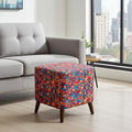 A square ottoman with a vibrant multicolor geometric pattern and dark wood legs, positioned in a modern living room next to a light gray sofa.
