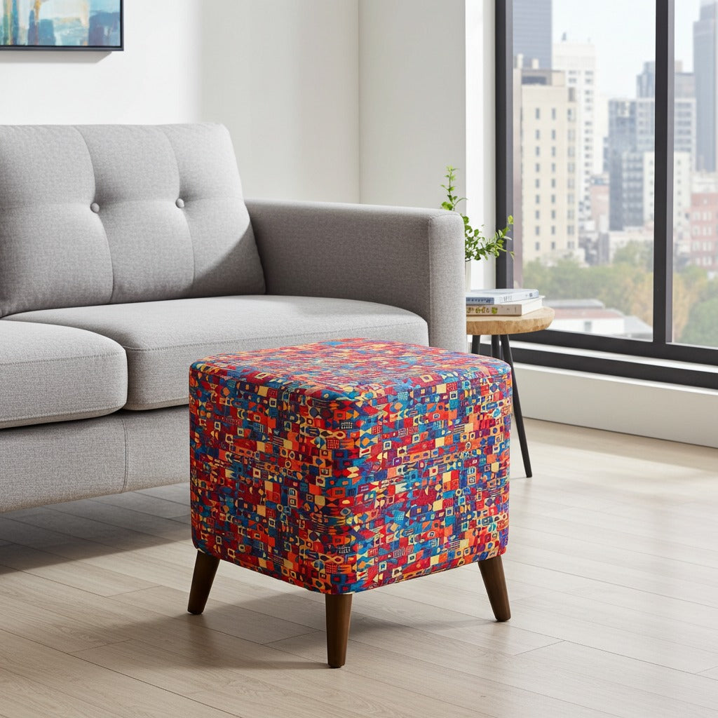 A square ottoman with a vibrant multicolor geometric pattern and dark wood legs, positioned in a modern living room next to a light gray sofa.