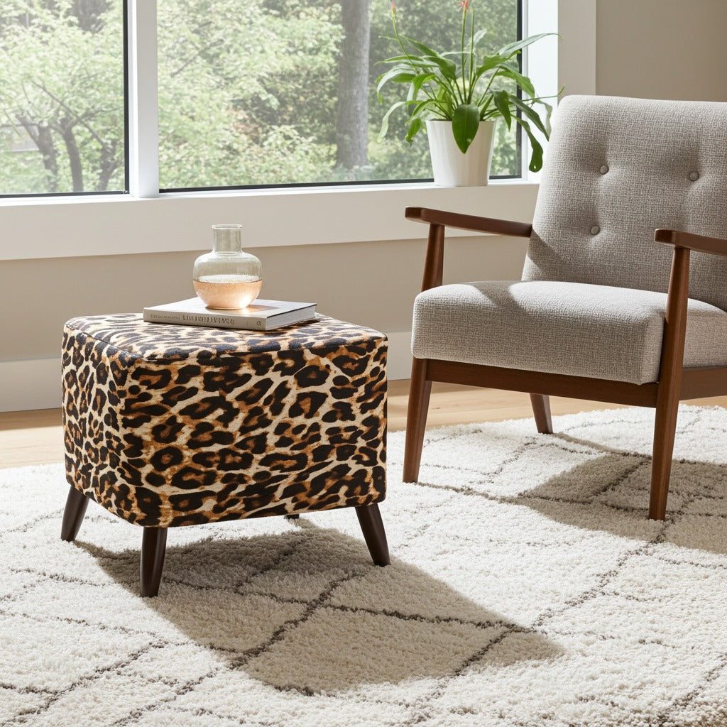 A leopard-print ottoman with dark wooden legs sits on a white patterned rug next to a light gray upholstered armchair in a bright room with a window and potted plant.