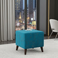 A square ottoman stool in bright turquoise blue fabric with a subtle gold floral pattern and dark brown wooden legs, styled in a modern room setting with a city window view.