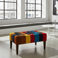 A rectangular tufted ottoman bench with colorful striped upholstery in yellow, orange, brown, blue, red, and black, supported by four dark wooden legs, shown in a modern, sunlit room.
