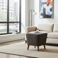 A modern living room scene featuring a dark brown marble-patterned ottoman with wooden legs in the foreground, next to a cream-colored sofa and a black floor lamp near a large window.