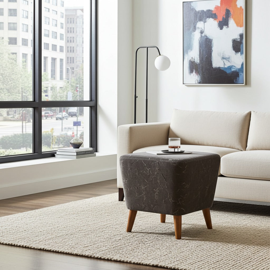 A modern living room scene featuring a dark brown marble-patterned ottoman with wooden legs in the foreground, next to a cream-colored sofa and a black floor lamp near a large window.