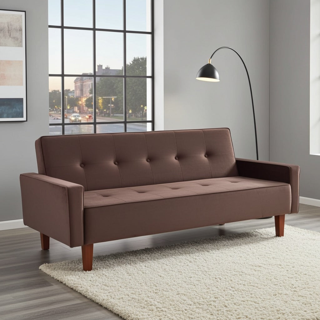 A brown upholstered futon sofa with button tufting on the back and seat, shown in a modern living room setting with a white shag rug, gray walls, a window, and a black floor lamp.