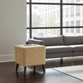 A square ottoman with a textured yellow and beige geometric pattern and dark wooden legs, styled in a modern living room next to a gray sofa.