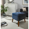 A blue tufted velvet storage ottoman with tapered wooden legs, styled in a modern living room setting.