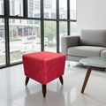 A square red upholstered ottoman with dark wooden legs, styled in a modern living room setting next to a gray sofa and a glass-top coffee table.