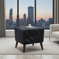 A square ottoman with a black marble pattern and tapered wooden legs, styled in a modern living room setting with a city skyline view in the background.