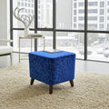 A square blue velvet ottoman with a gold geometric crackle pattern and dark wooden legs, styled on a beige shag rug in a modern room with large windows.