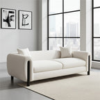 A modern cream bouclé loveseat sofa with black legs, styled in a bright contemporary room with a city view window background.