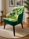 Green armchair with tropical leaf pattern in a room with plants and framed pictures.