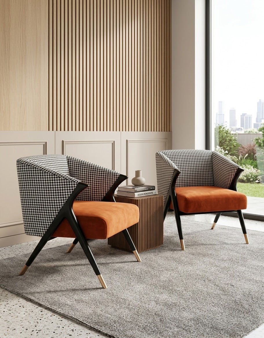 Two modern accent chairs with black-and-white houndstooth fabric backs and orange velvet seats, arranged on a gray rug in a contemporary room with wood slat wall paneling and a large window.