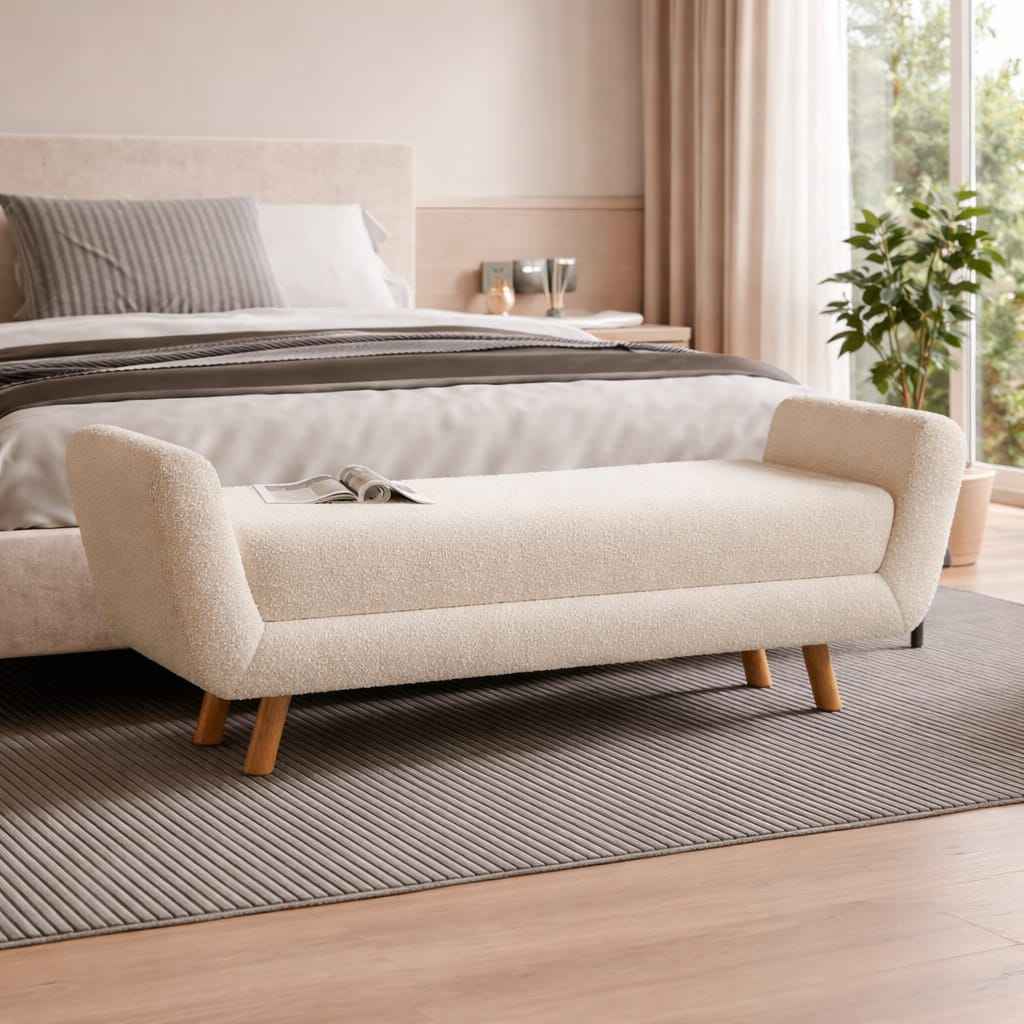 Beige upholstered bench in a bedroom setting with a bed and window in the background.