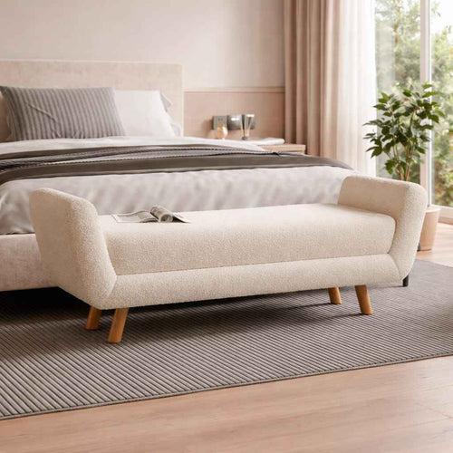 Beige upholstered bench in a bedroom setting with a bed and window in the background.