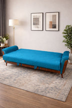 Blue futon sofa in a room with a lamp, plants, and framed art on the wall.