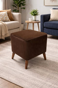 Brown ottoman in a living room setting with a beige sofa, blue armchair, and small table.
